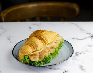 Croissant stuffed with turkey slices, cheese, and crisp lettuce on marble table with copy space. ideal for breakfast promotions, culinary websites, food blogs. Ham and cheese croissant