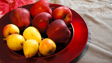 Yellow Sicilian pears and red Tyrolean apples on a festive plate, gray tablecloth, red and yellow, warm colors, honey apples, festive background, side view, Italy