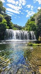 Fototapeta premium Beautiful Waterfall Cascading in a Lush Mountainous Landscape on a Sunny Day. Concept of Natural Beauty, Scenic Outdoors, Tranquility, and Refreshing Environments. Vertical