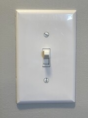 A white on and off light switch (with face plate) on a light grey wall.