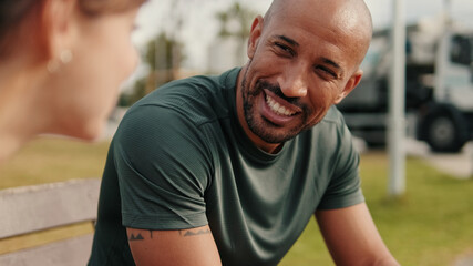 Close-up side view of people in sportswear cheerfully talking and sitting on a park bench, two...