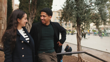 Happy young couple laughing and chatting in an urban setting with trees and blurred background