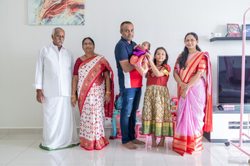 Obraz premium An Indian family wearing traditional and casual costumes spends time with their baby, girl and grandparents in a high-rise apartment building in Kuala Lumpur, Malaysia. June 2024