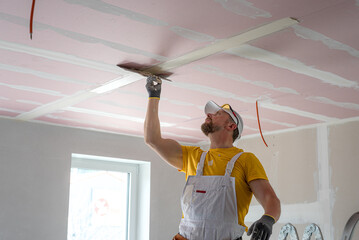 The worker make a plasterboard ceiling. He does taping plaster drywall ceiling joints. He is using...