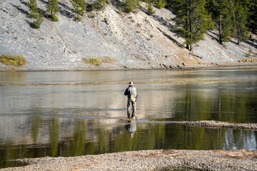 a fly fisherman in waders stood mid-river, using a two-handed rod to cast a fly line