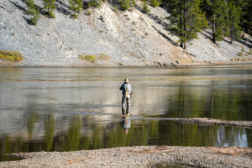 a fly fisherman in waders stood mid-river, using a two-handed rod to cast a fly line