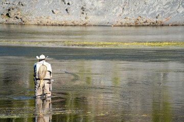 a fly fisherman in waders stood mid-river, using a two-handed rod to cast a fly line