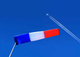 a passenger plane with vapour trails high in the blue sky and french windsock