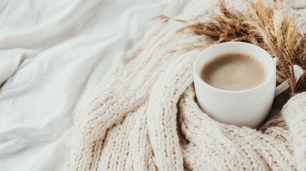 A warm coffee cup rests on a textured blanket, nestled among dried plants, creating a cozy and comforting scene perfect for a quiet, restful moment of solitude.