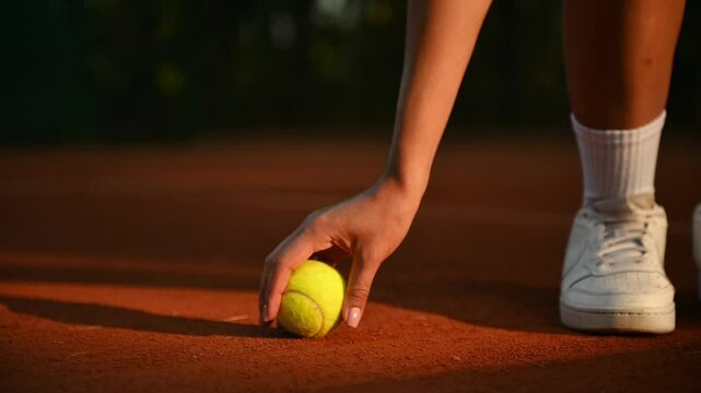 A tennis player picks up a ball from a close-up map. Levushka is playing tennis in the park. sports equipment in the form of a tennis ball lies on the court. 