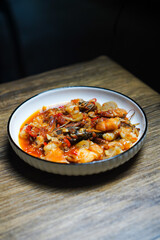 A bowl of food with a red sauce and a few pieces of meat