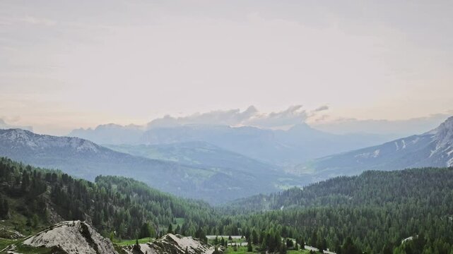 vol de drone au coucher de soleil a l'entr&eacute;e des dolomites avec une couleur ros&eacute;e avec les montagne en arriere plan derriere la foret