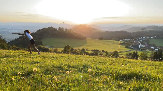 Little girl doing Cartwheel gymnastics sideways rotary movement on green grass hills at sunset time near Zilina town in Slovakia. Happy childhood moments or outdoor time spending concept 4K footage.