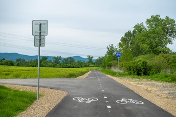 Asphalt cycling path in the country marked with symbols on the road and vertical signs.