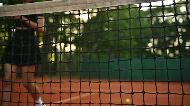 A tennis player plays sports in the park. The girl runs to the net on the tennis court. Tennis net on the court in the park. 