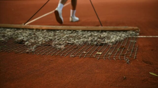 A tennis player clears the dirt surface on the tennis court . Tennis sports equipment in close-up. Preparing the tennis court for training. 