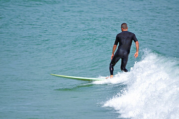 A surfer seen from behind in a black wetsuit surfing a wave in the ocean in Florida