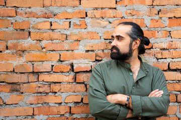 Obraz premium A dark-haired, bearded man of Dominican appearance in a green shirt against a brick red wall. The man near the wall looks away. Empty space for text. High quality photo