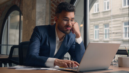 Obraz premium Tired stressed sad male guy Arabian man office employee tap keyboard on laptop boring online work in office alone Indian businessman exhausted lazy burnout overwork headache stress business problem