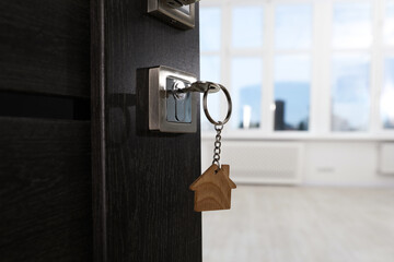 Open door with key and house shaped keychain, closeup. Space for text
