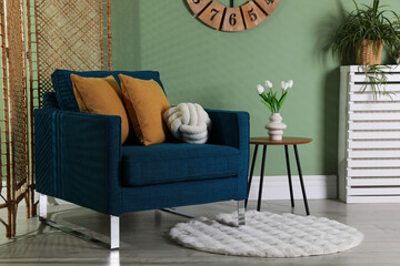 Folding screen, comfortable armchair with pillows and side table in room