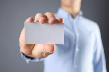 Man holding blank business card on grey background, closeup. Mockup for design