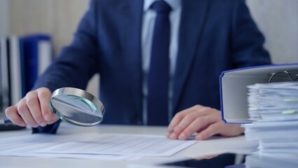 Businessman is carefully examining financial documents with a magnifying glass, highlighting the importance of thorough analysis in business. Audit and taxes