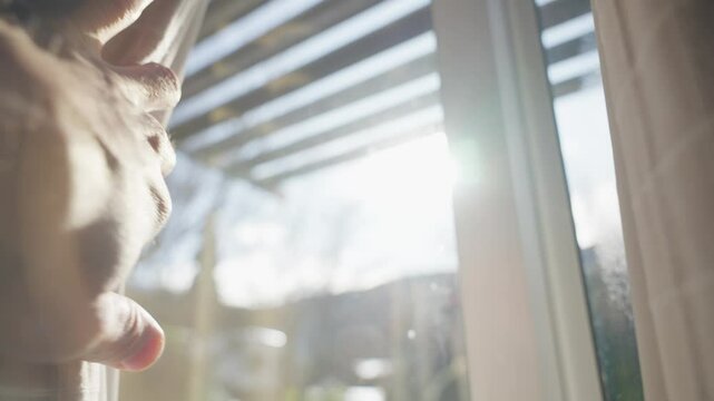 Hand slowly reaching towards a window curtain and open it to reveal sunlight. Dark room as hand of a man pushes heavy drape to let the sunlight shine inside. Bright sunny day outside. Hope and energy