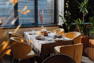 Elegant restaurant table setup with natural sunlight, cozy chairs, and stylish decor for dining