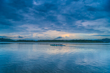 Before the rain sunrise waterscape with rowers on the bay © Merrillie