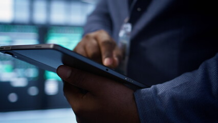 Software developer doing yearly maintenance using tablet to prolong data center equipment life span. Extreme close up of worker in server hub monitoring server infrastructure using device, camera B