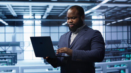 Programmer in data center typing on laptop, running error checking utilities. IT professional in server room looking for network issues affecting rigs performance using digital device, camera A