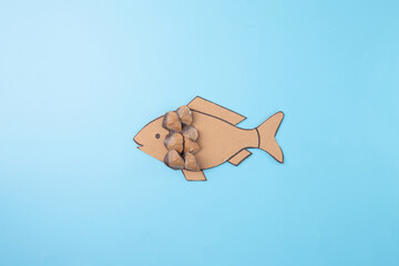 cardboard cut into the shape of a fish, with small pine cone scales glued onto it. step in DIY...