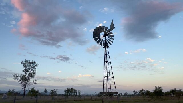 Silhouette of a tall wind pump turning at sunset in a remote farm in the outback of  Queensland Australia