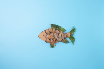 a paper cut out of a fish on a blue surface, conceptual art, brown seed scales, DIY dry leaf clip...