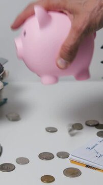 Vertical video. Coins pour from a piggy bank onto a table with financial tools, underscoring budgeting