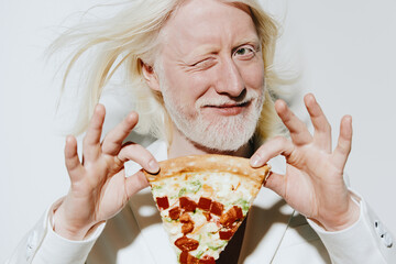 cheerful man with long white hair winking and holding a slice of pizza, on a plain light...