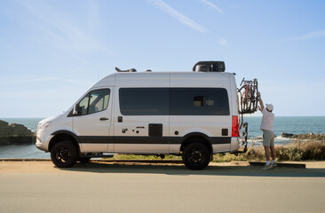 Naklejka premium Man taking down his bike from mobile home while parked at Asilomar Beach in Pacific Grove, California. Wide shot