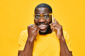 Happy young man with glasses talking on the phone, expressing joy and excitement, against a bright...