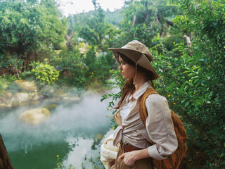 A woman in a hat standing near a river with steam coming out of the water