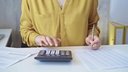 Businesswoman with yellow blues is using dark calculator and taking notes in her office. Taxes and...