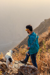 hombre joven parado a orillas de una montaña mirando al frente acompañando e su perro 