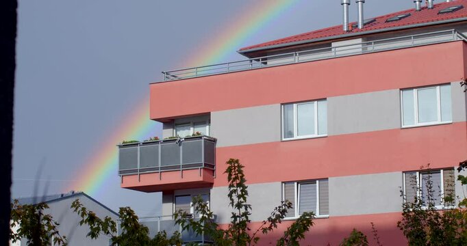 A beautiful and vibrant rainbow gracefully arches over a pink modern building beneath a dramatic and cloudy sky light phenomenon in the sky