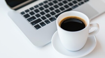 A close-up of a white coffee cup filled with black coffee beside a laptop, on a clean, minimalist desk.