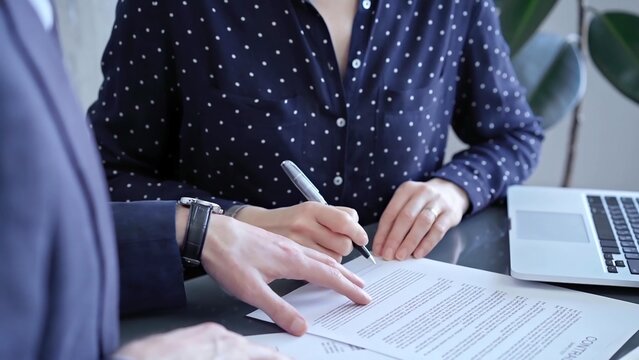 Detailed view of two business people or lawyers signing a contract with a laptop nearby