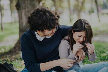 Fototapeta premium A young couple is seated in a sunny park, sharing an emotional moment. The student is comforting his partner, illustrating love and support. The vibrant greenery in the background adds to the serene