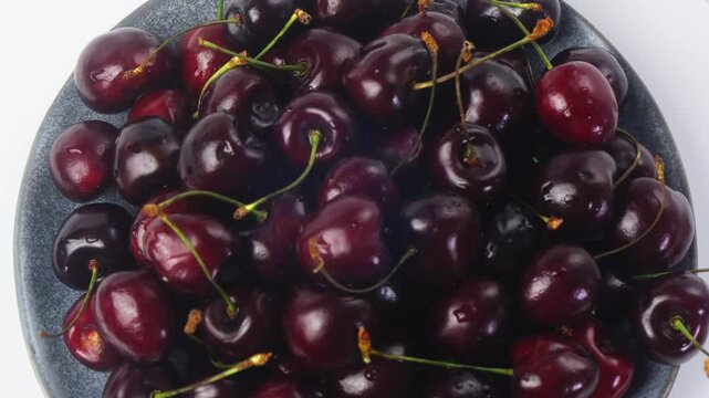Scattering of ripe dark red cherries with branches rotating in a circle. Medium plan