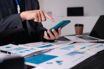 businessman sits at his office desk, analyzing financial documents and graphs on his laptop. paperwork, calculator, and charts, he strategizes investments, audits, tax planning for success.