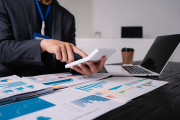 businessman sits at his office desk, analyzing financial documents and graphs on his laptop. paperwork, calculator, and charts, he strategizes investments, audits, tax planning for success.