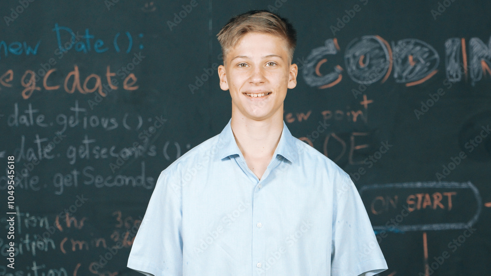 Poster smiling teenager looking at camera while standing at blackboard with engineering code or prompt writ
